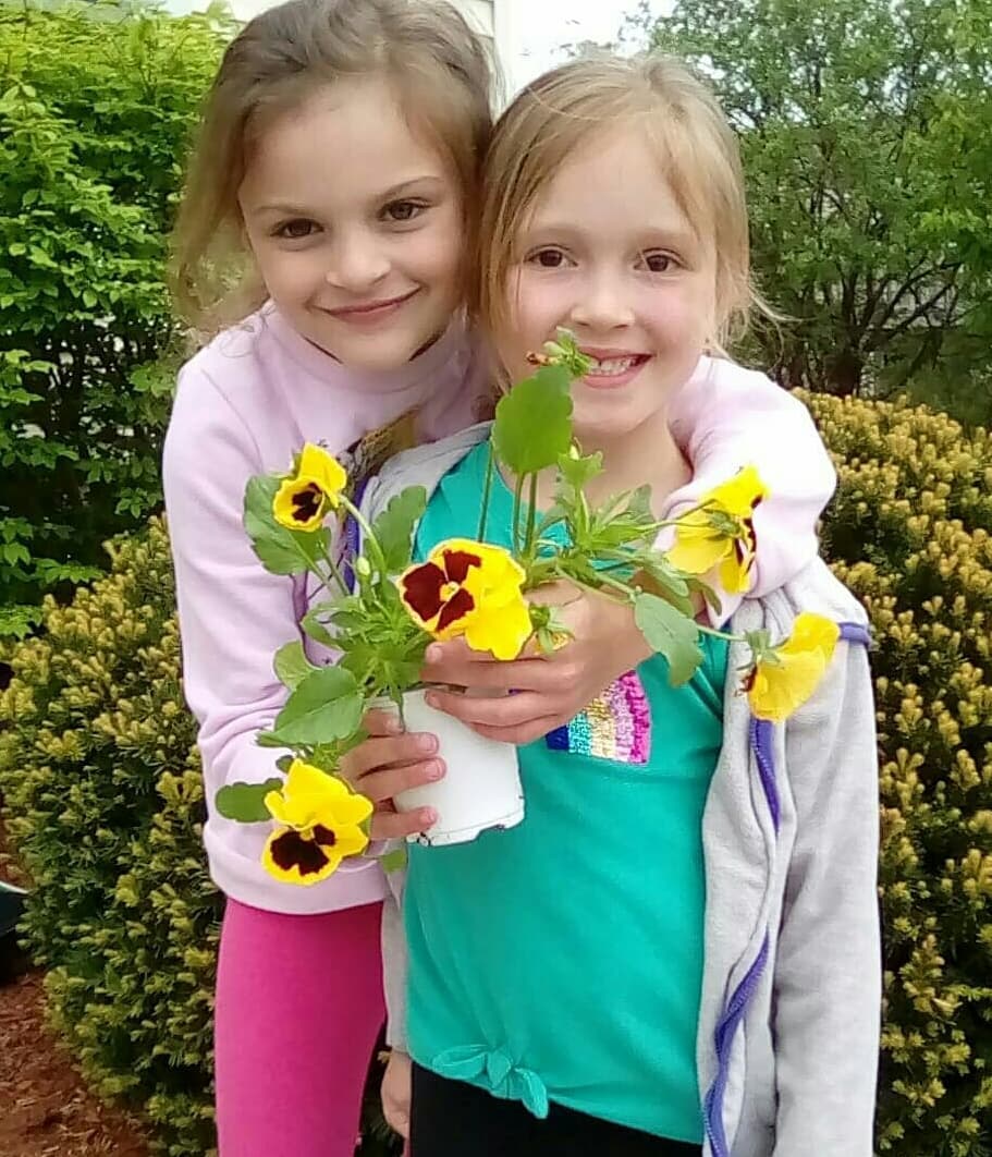 Two young girls holding a potted flower at Care A Lot Child Care Center